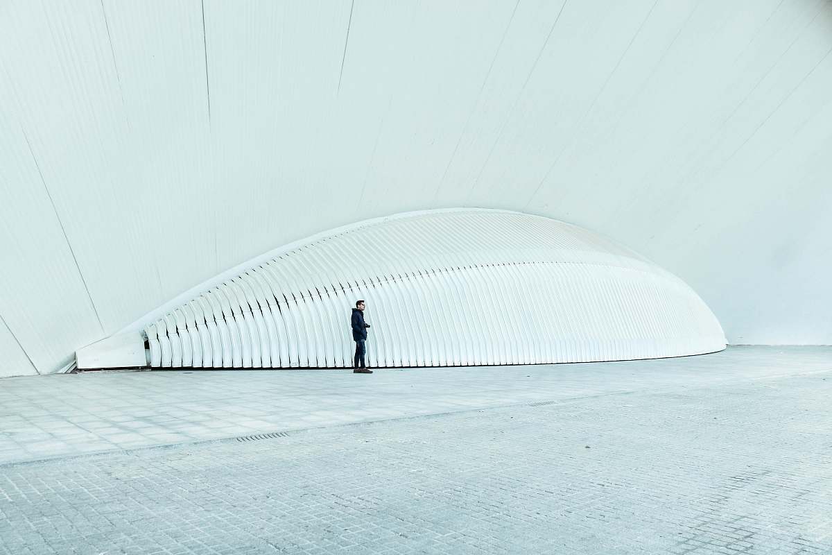 grey person wearing black long-sleeved top standing near white structure spain